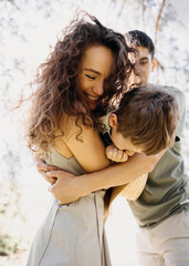 Loving parents hugging their young son outdoors on a sunny day