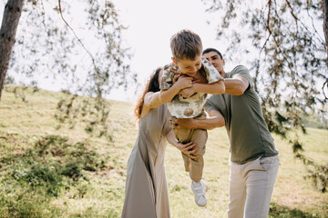Parents playfully swinging their son outdoors on a sunny day