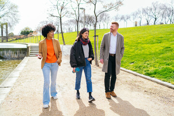Three young professionals enjoy a conversation while walking together on a path in a sunny city park