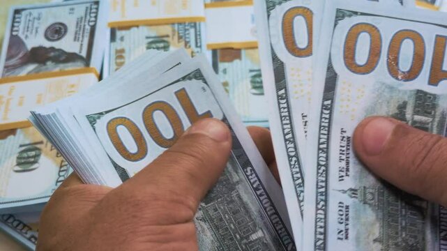 A man counts hundred-dollar bills, with even more cash in the background.