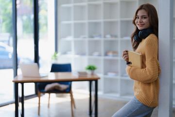 Smiling student leans against pillar in study room with a book and headphones.