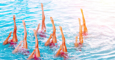 Synchro swimmers perform an elegant routine in a bright blue pool under the sun