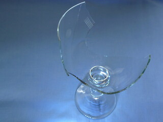 A broken wine glass with a wedding ring inside, placed on a blue background. Conceptual image symbolizing relationship breakup, vulnerability, betrayal, or loss of love.