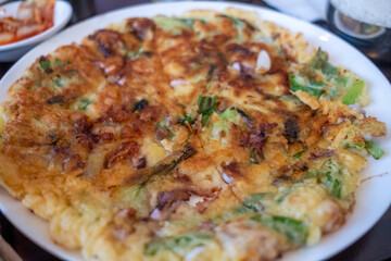 Overhead view of a haemul pajeon Korean seafood pancake served on a white ceramic plate with dipping sauces nearby