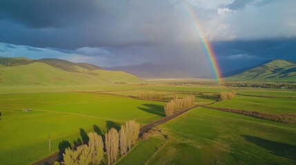 Vibrant rainbow arching over green valley and mountains after passing storm
