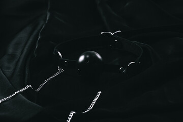 Black ball gag with metal chains on dark fabric surface