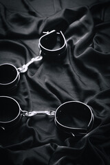 Elegant black leather handcuffs on dark fabric creating dramatic contrast