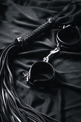 Black leather handcuffs and whip on dark fabric