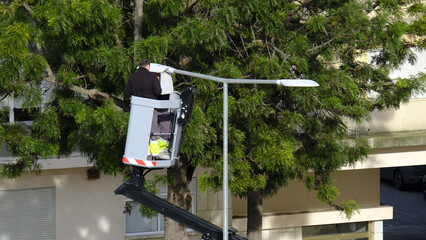 Worker in lift platform check street lamp in residential area on sunny
