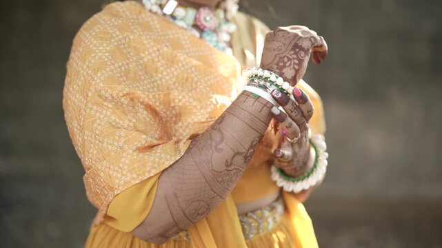 Dressed in a vibrant yellow haldi outfit, the girl glows with joy. Her hands adorned with colorful bangles shimmer in the sunlight, capturing the festive, playful, and traditional spirit of the ceremo