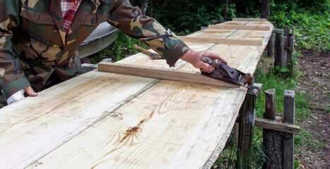 Crafting wood surfaces under natural light with a hand planer in a forested area during daytime