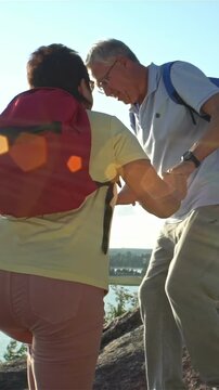 Active senior couple hiking hand in hand on a rocky hill near the seaside in Finland. Elderly man and woman wearing backpacks, enjoying outdoor adventure, support and companionship in old age.