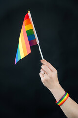 Woman with wedding ring holding rainbow flag on black background. 