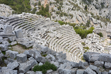 View of a partially ruined ancient amphitheater with a panoramic mountain backdrop. A unique...