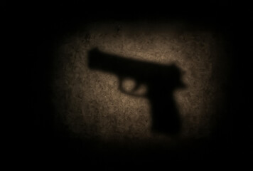 Dimly illuminated pistol silhouette cast on textured surface under a dramatic light, symbolizing fear, crime, and hidden violence.