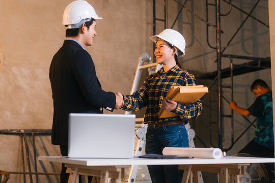 Asian male and female engineers examine construction blueprints and review material costs steel and limestone, preparing competitive bid proposal for building project in collaboration with project