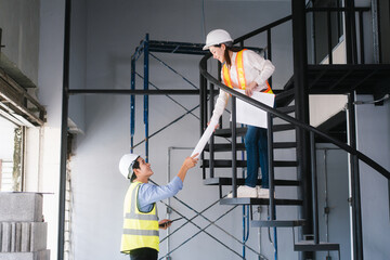 Asian male and female engineers wearing safety vests and helmets inspect structural elements,...