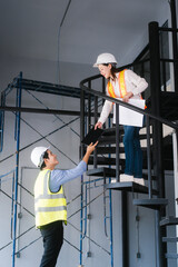 Asian male and female engineers wearing safety vests and helmets inspect structural elements,...