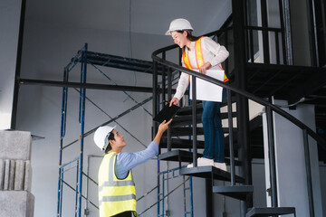 Asian male and female engineers wearing safety vests and helmets inspect structural elements,...