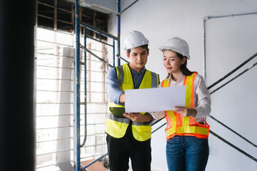 Asian male and female engineers wearing safety vests and helmets inspect structural elements,...