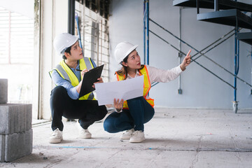Asian male and female engineers wearing safety vests and helmets inspect structural elements,...