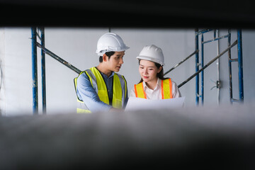 Asian male and female engineers wearing safety vests and helmets inspect structural elements,...