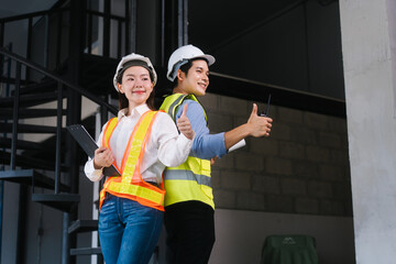 Asian male and female engineers wearing safety vests and helmets inspect structural elements,...
