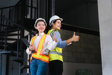 Asian male and female engineers wearing safety vests and helmets inspect structural elements,...