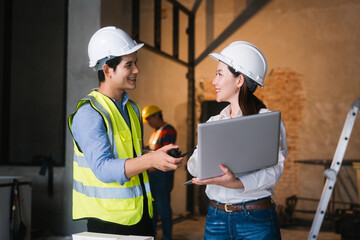Asian male and female engineers wearing safety vests and helmets inspect structural elements,...