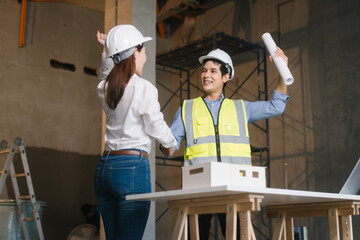 Asian male and female engineers wearing safety vests and helmets inspect structural elements,...
