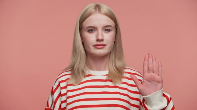 Serious woman making stop gesture with raised hand on pink background