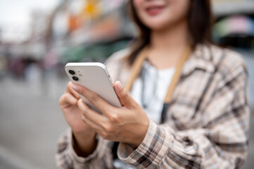 Close up of tourist woman in scotch pattern shirt checking her phone standing by the road in market.