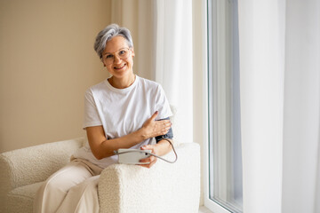 An elderly, mature lady with gray hair makes a health checkup and measures blood pressure
