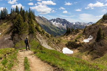 Eine Wanderin auf einem Bergpfad über grüne Hänge mit Blick in die weite, schneebedeckte...