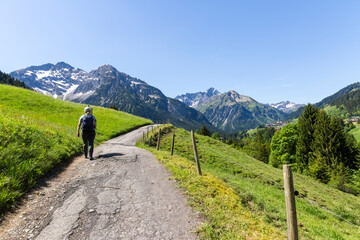 Eine Wanderin auf einem Bergpfad über grüne Hänge mit Blick in die weite, schneebedeckte...