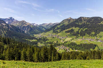 Alpent&auml;ler mit D&ouml;rfern Mittelberg, Hirschegg und Riezlern inmitten umliegenden Bergen, eingerahmt von B&auml;umen im Kleinwalsertal, &Ouml;sterreich, Europa