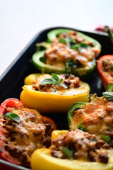 Close-up of vibrant stuffed bell peppers filled with seasoned ground beef, bulgur, and melted cheese. The dish is baked and served in a red baking dish placed on a blue rustic  food background. yummy