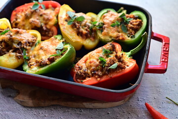 Close-up of vibrant stuffed bell peppers filled with seasoned ground beef, bulgur, and melted cheese. The dish is baked and served in a red baking dish placed on a blue rustic  food background. yummy