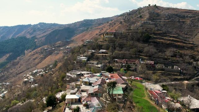Zoom in of a mountain village in Murree with rooftops, trees and steep terrain