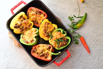 Close-up of vibrant stuffed bell peppers filled with seasoned ground beef, bulgur, and melted cheese. The dish is baked and served in a red baking dish placed on a blue rustic  food background. yummy