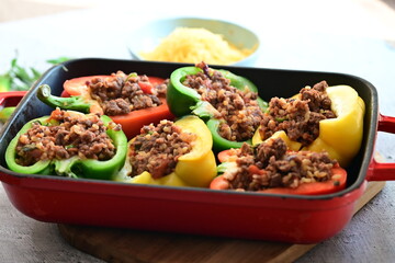 Close-up of Mediterranean-style stuffed bell peppers arranged in a red baking dish, ready for the oven. This homemade meal scene on a light background captures the essence of fresh, flavorful cooking