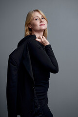 Confident Woman Posing in Black Outfit Holding Jacket Over Shoulder..
