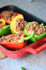 Close-up of Mediterranean-style stuffed bell peppers arranged in a red baking dish, ready for the oven. This homemade meal scene on a light background captures the essence of fresh, flavorful cooking