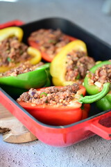 Close-up of Mediterranean-style stuffed bell peppers arranged in a red baking dish, ready for the oven. This homemade meal scene on a light background captures the essence of fresh, flavorful cooking