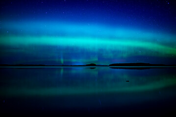 Northern lights dancing over calm lake in north of Sweden.
