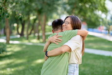 Mother Hugging Son in a Sunny Park with Greenery All Around.
