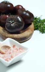 Black tomatoes and pink salt in a saucer on a light background, vertical shot