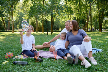 Fototapeta premium Family Enjoying a Relaxing Picnic Day Together Making Soap bubbles Outdoors in the Park