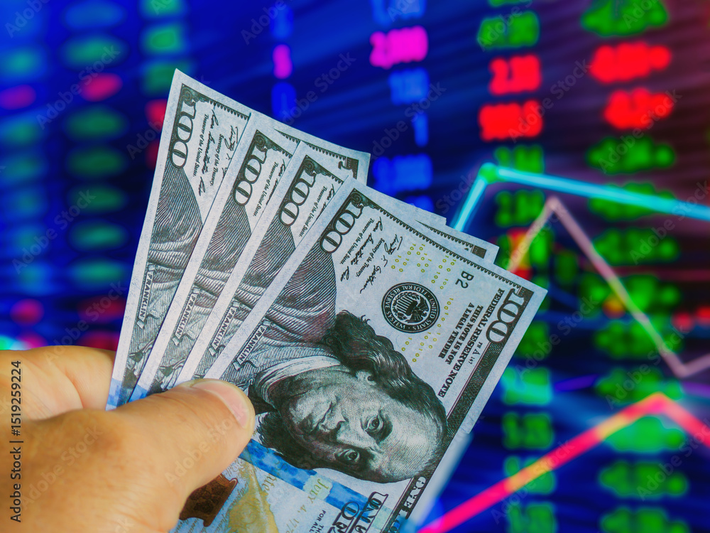 Poster a hand holding several hundred-dollar bills is positioned in front of a colorful stock market displa