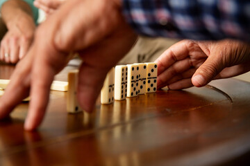 Fototapeta premium Close-up of elderly father's hands placing dominoes on the table during a quiet game with his adult son - a tender moment of age and connection.